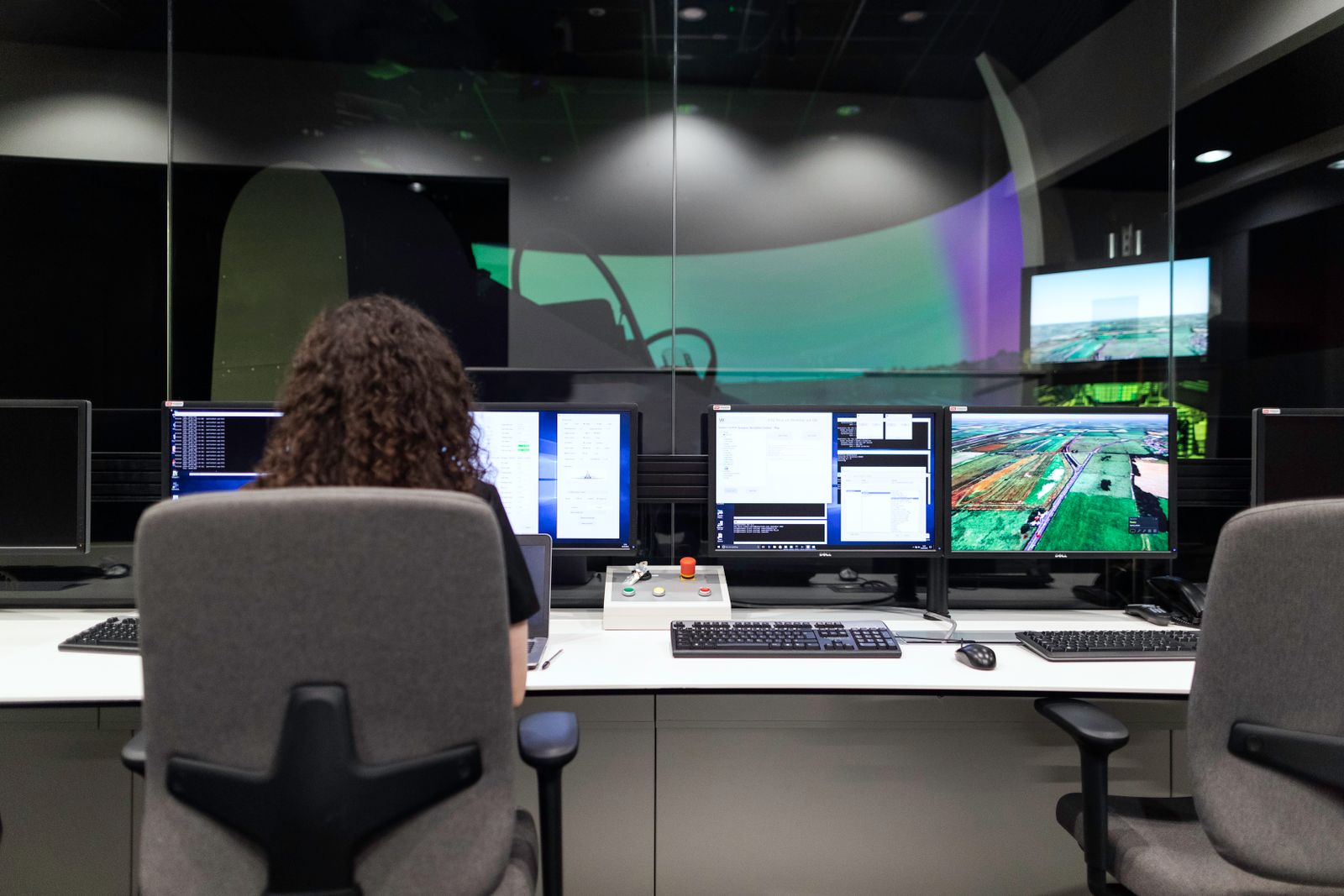 Engineer at a multi-monitor desk overlooking a flight simulator rig through glass